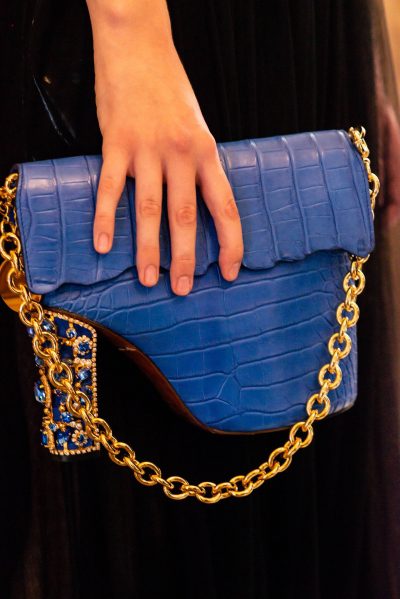 A person holding onto a blue purse with gold chain.